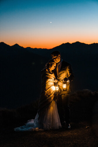 a bride and groom snuggle under a blanket at dusk on hurricane ridge in olympic national park after their elopement