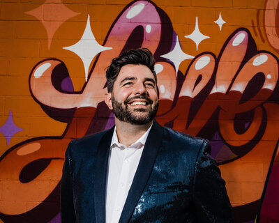 A person smiling and standing in front of a mural.