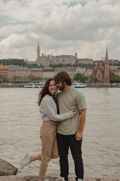 Couple standing by the Danube river in Budapest smiling at the camera