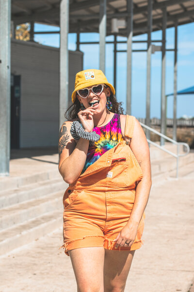 Model wears overalls and bucket hat while posing with a lollipop in Bradenton, Florida