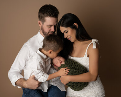 Austin newborn photographer captures tender family moment with parents and big brother snuggling baby during studio session