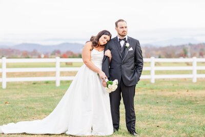 Bride wearing a Maggie Sottero gown and groom wearing a black tuxedo posing together sweetly in a fall field on their wedding day.