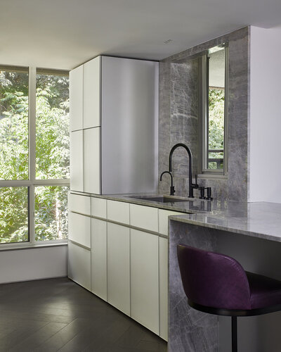 A kitchen sink area featuring a marble countertop and backsplash, white back painted cabinetry, and a large window