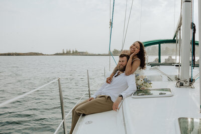 bride and groom on a sailboat sitting and snuggled together smiling. captured by a north shore elopement photographer