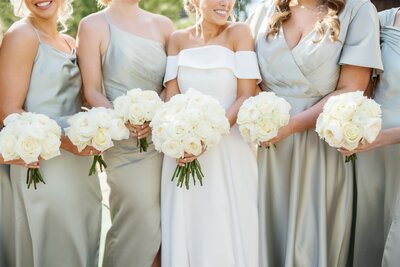 Bride with her bridesmaids in pale green dresses smiling and holding round white bouquets