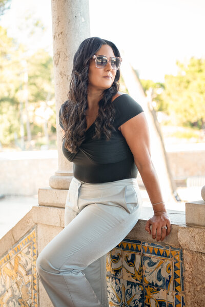 Asmahan walking up tiled steps in Lisbon wearing a black top, silver pants, and sunglasses, holding a vibrant pink handbag