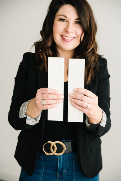 A woman in a black blazer holds up two different white paint samples