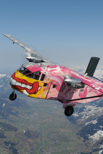 Eine Pink Skyvan in leuchtendem Rosa fliegt majestätisch durch den klaren blauen Himmel. Das Bild zeigt die beeindruckende Größe und einzigartige Farbgebung des Flugzeugs in Aktion.