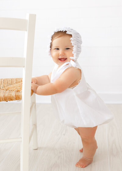 8 month old sitting on blue fabric wearing overalls looking at the camera