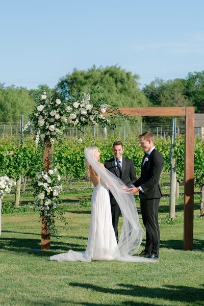 Charming wedding ceremony arch designed by Leigh Florist, adorned with delicate flowers, lush greenery, and a soft color palette perfect for an outdoor celebration.