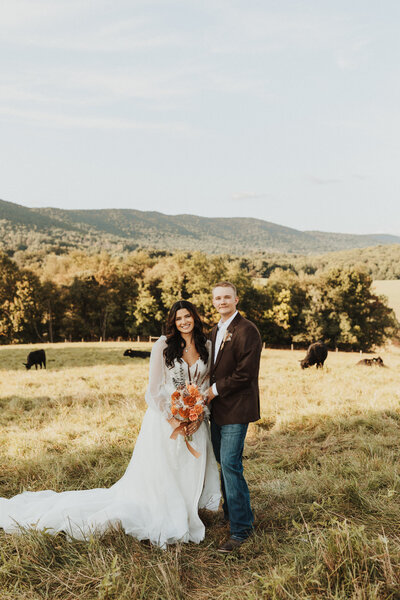 bride and groom standing in a field embracing and smiling with cows in the background
