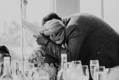 Father cuddling his newlywed daughter during speeches at a high-end wedding