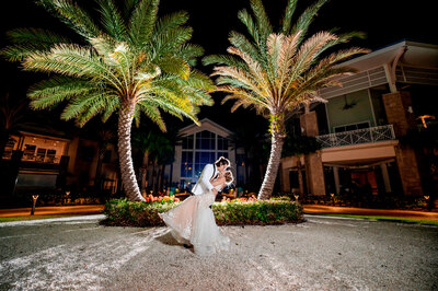 couple kissing night wedding outfits under two palm trees