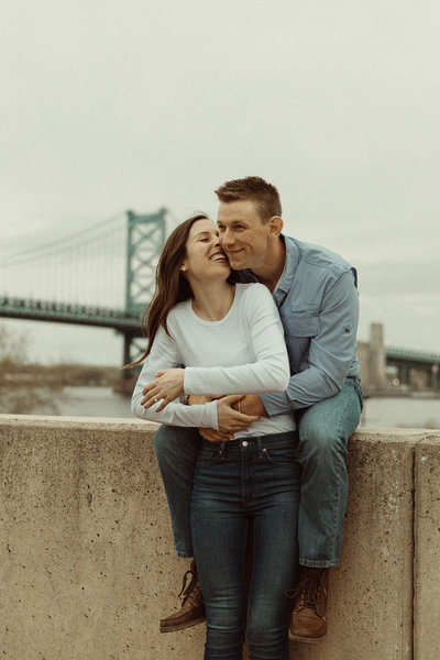 Couple sits in front of the Benjamin Franklin Bridge in Philadelphia waterfront