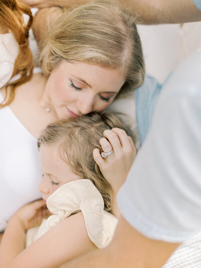 Blonde mother lying in husband's lap embraces blonde daughter's head taken by Little Rock family photographer Bailey Feeler Photography