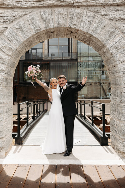 Bride and groom standing under stone arch and smiling