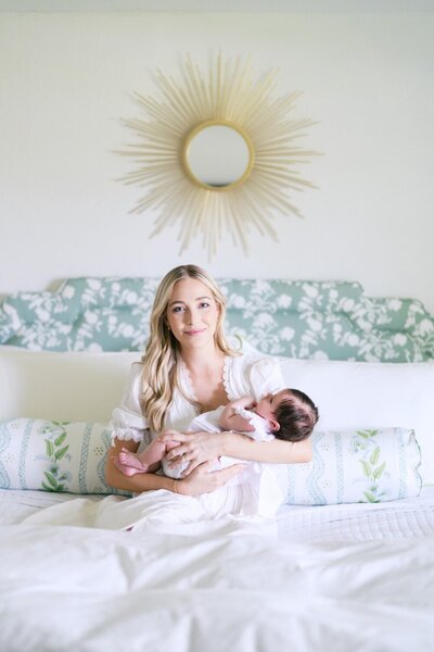 Mother sitting on bed cradling baby during a natural light newborn portrait session