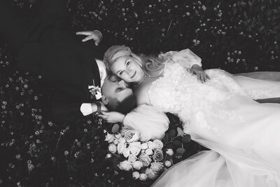 Bride and groom lying in a field of flowers, captured in a romantic black and white wedding portrait in Gainesville, Florida by Salt + Heart Photography