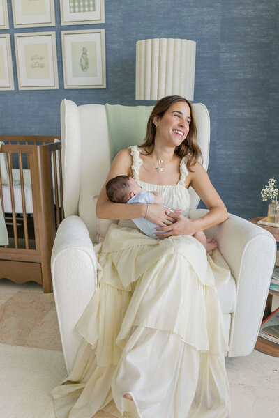 Smiling mom nursing her newborn in a soft-toned nursery chair at a brickell home.