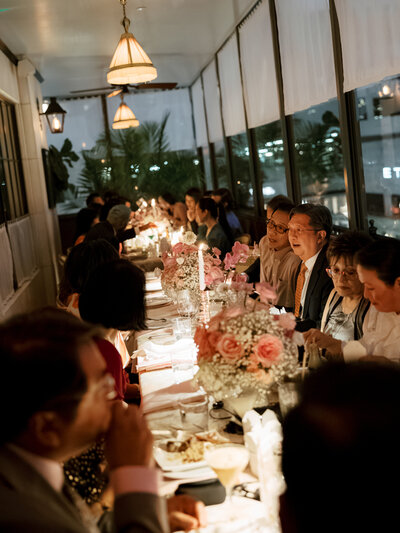 April M Payne Photography captured a warm, intimate wedding reception with guests enjoying dinner around a beautifully set table, featuring floral arrangements and soft lighting, creating a cozy, inviting atmosphere.
