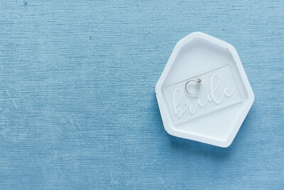Flat lay photo of a wedding ring on a nameplate that says “bride.”