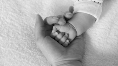 Parent holding her baby's tiny hand, symbolizing warmth, connection, and new beginnings