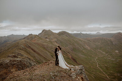 Bride and groom kiss on cliff edge in the San Juan Mountains
