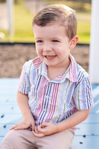 Kellen in a rainbow striped collared shirt smiling into the distance.