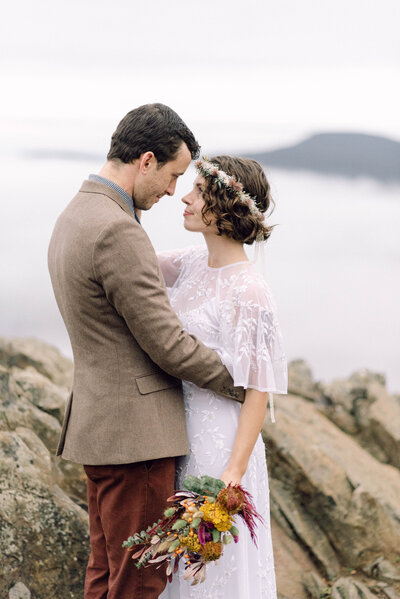 Cinematic wide shot of the couple embracing on the summit, with soft focus and natural light.
