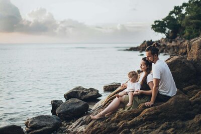 Eine Familie sitzt auf Felsen am Meer.