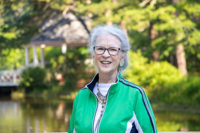 Fran Stewart author wearing green jacket standing by park lake