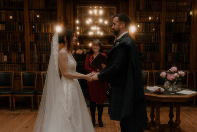 Bride and groom exchanging vows inside the Royal College of Physicians Library in Edinburgh, captured in a cinematic fine art style by Scottish wedding photographer Aly Robinson.