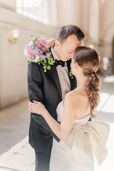 Bride stands forehead to forehead with groom while her bouquet is draped over his neck