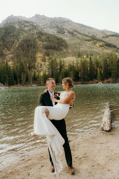 photo of groom holding bride next to a lake taken by Grand Teton elopement photographer