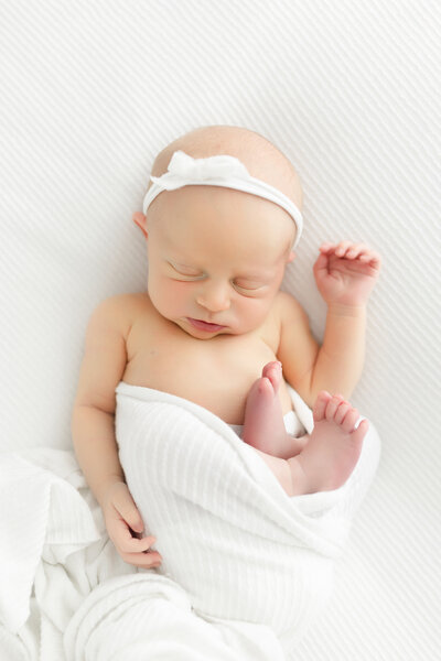 A newborn baby girl laying on a white blanket sleeping during her newborn photography session.