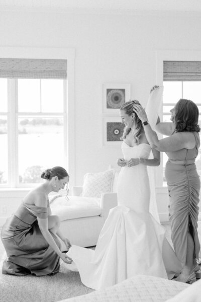 Beautiful black-and-white moment of a bride getting ready at a private estate in Newport, Rhode Island. The bride is assisted by her bridesmaids as they help her prepare for the big day, capturing the intimate and emotional moments of wedding preparation. Felisha, a New England-based destination wedding photographer, specializes in capturing timeless moments in Newport, Rhode Island, New England, and worldwide locations.