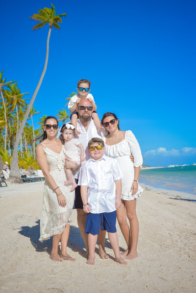 Photo of the Stackewicz family, the family of the woman who owns KC Entities Roofing and Siding, on a beach with a palm tree and the ocean in the background and a blue sky