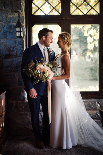 Bride wears romantic Alexandra Grecco gown with a cape, standing in castle room in VT