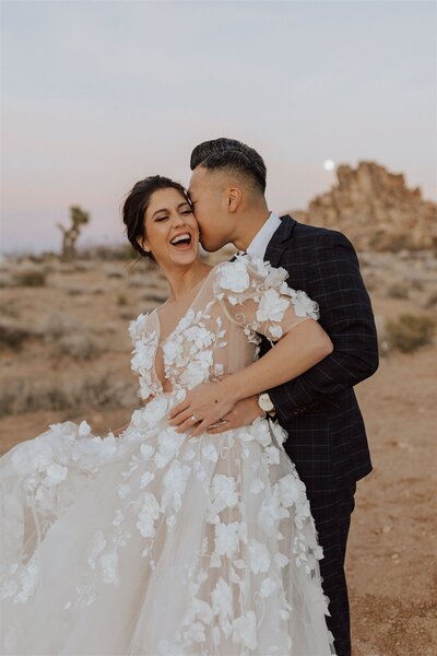 groom kissing brides cheek in a desert