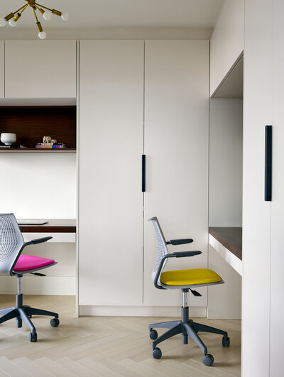 A bright and minimalistic workspace featuring white cabinetry and colourful chairs