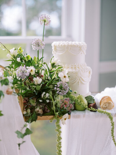Modern white two-tiered wedding cake decorated with bright green, white, and light purple florals designed by local North Carolina florist.