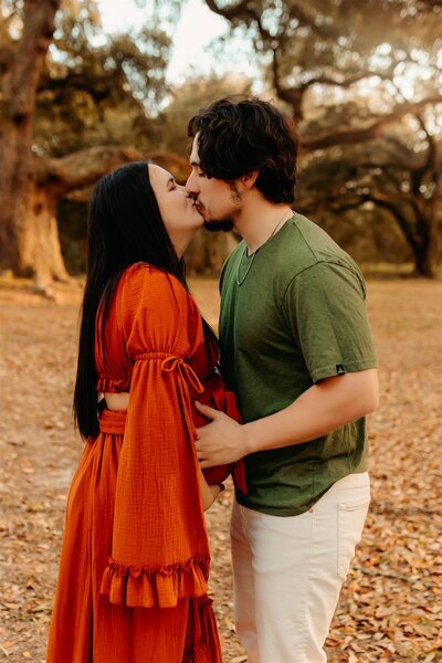 Couples maternity photography in Dayton TX - expecting parents sharing kiss outdoors beneath oak tree