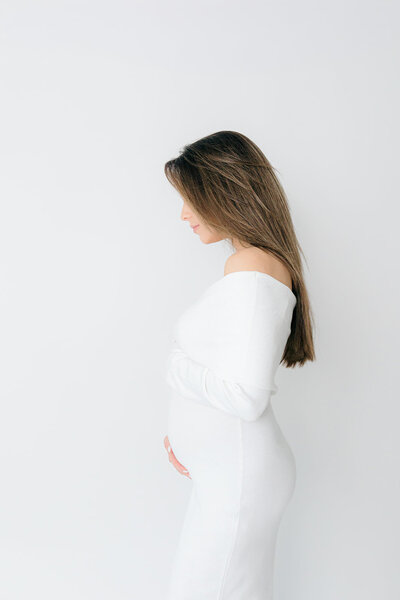 Pregnant woman with white dress posing for a maternity photo session in Laura Mariani's studio in Boulder CO