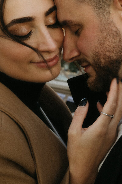 Couple snuggles together on the Brooklyn Bridge in New York City, NY at sunrise while the wind blows through the woman's hair, by Andrea-Marie Photography