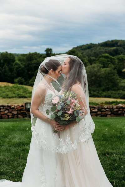 Two brides kiss underneath wedding veil