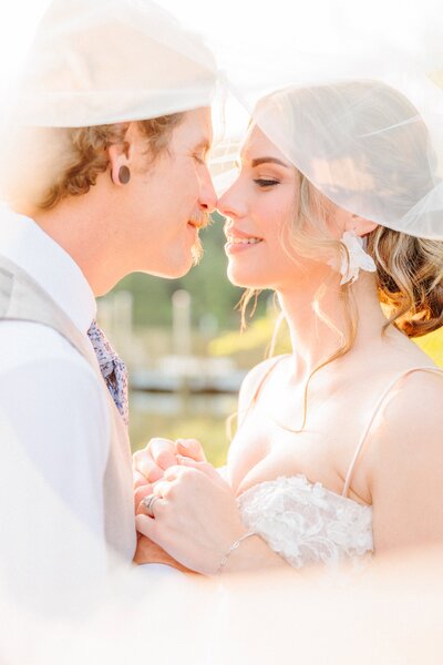 A couple kisses under a wedding veil.