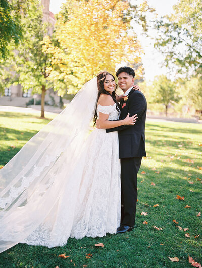 A wedding portrait photographed on film of a couple smiling at the camera, autumn leaves falling around them in Denver, Colorado.