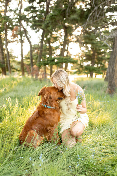 Young lady kisses the top of her dog's head  while holding a bouquet in her hand.