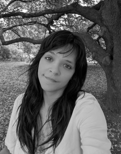 Black and white photo of woman with long, black hair and bangs wearing a shite long sleeve and smiling at the camera.