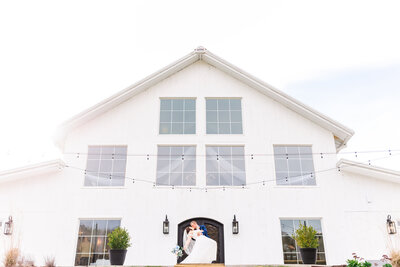bride and groom kissing in front of a barn wedding venue